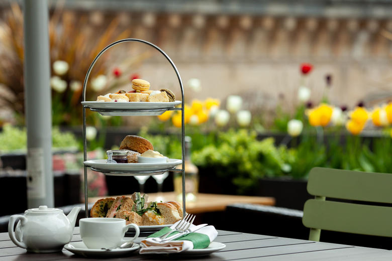 A tower of cakes, sandwiches and scones alongside teacup and teapot