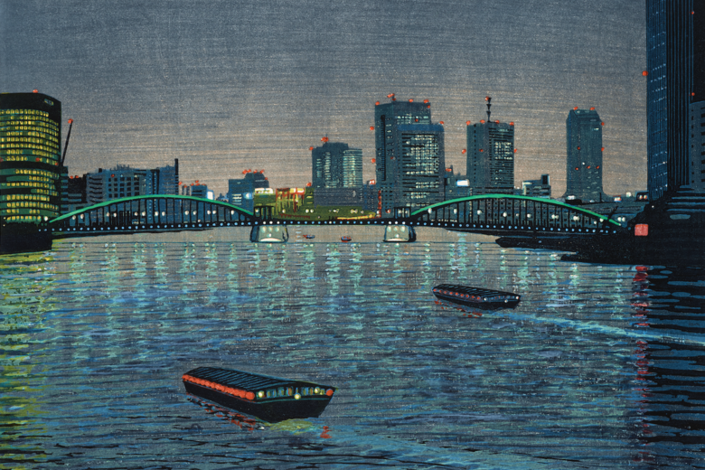 A view of a city by the water at night, with boats passing in the foreground