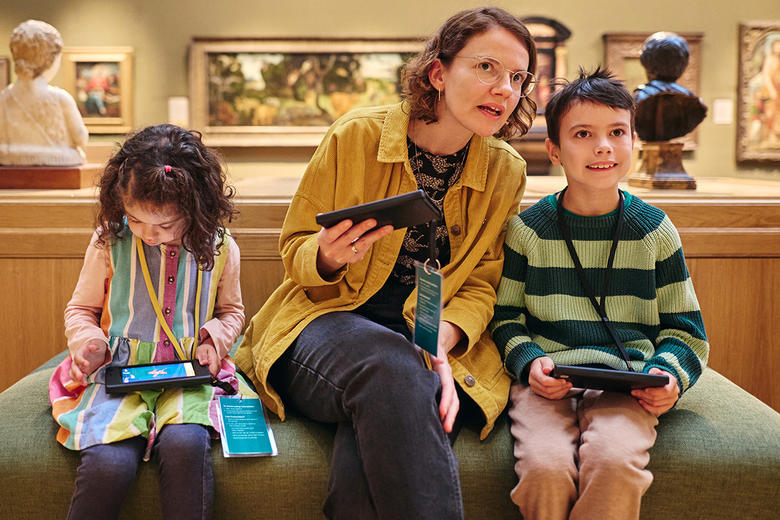 Mum and her daughter and son sitting on the bench in the gallery with the Ashmolean Adventure devices