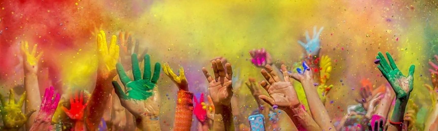 Colourful powders fill the air, and hands covered in powder and paint reach upwards, as part of Holi celebrations