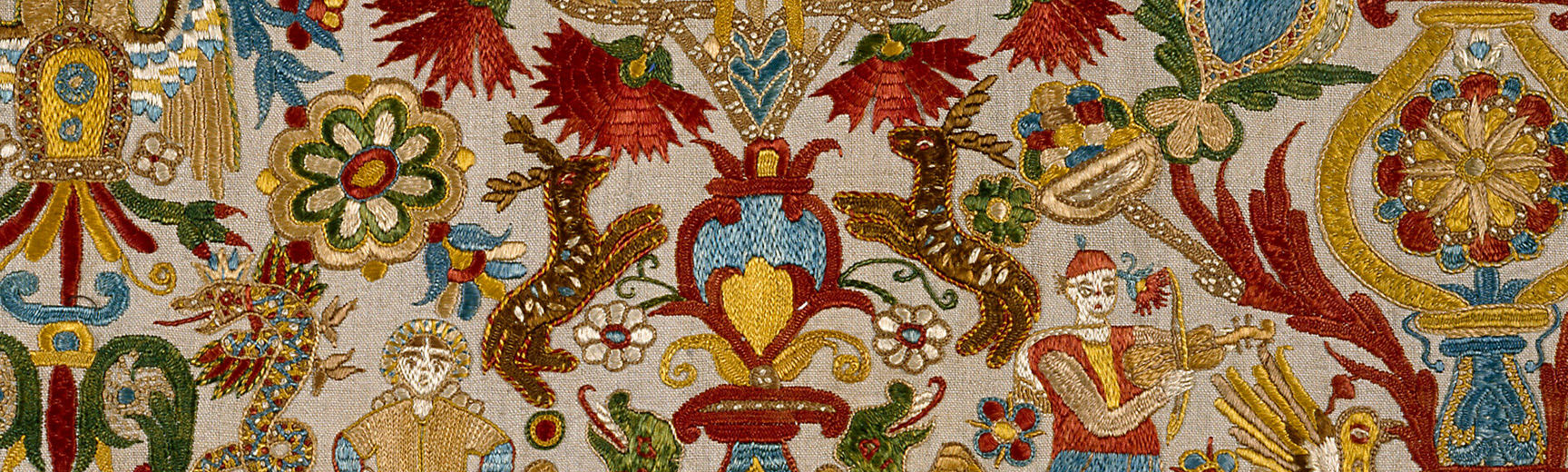 Detail of richly coloured and patterned embroidered cushion cover from Crete with flowers, figures and stags, in golds, blues and reds