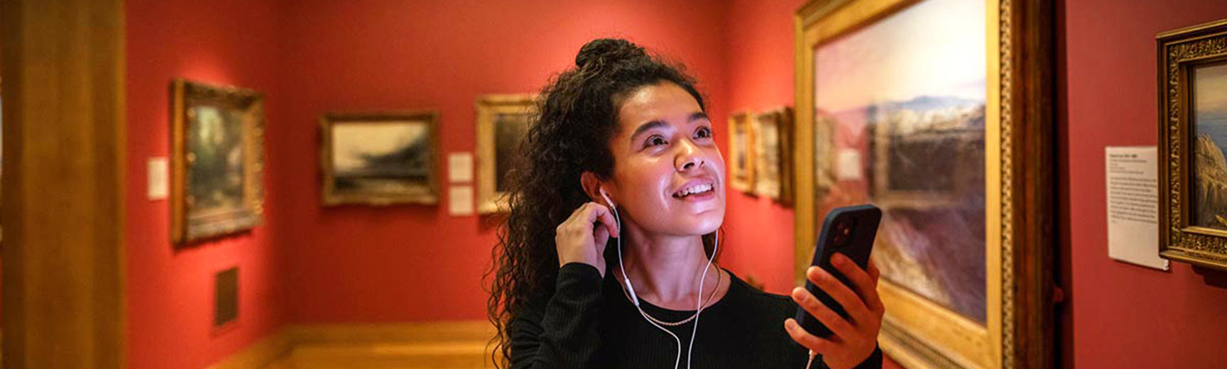A visitor with headphones and her phone listening to the Highlights Audio Tour in the galleries 