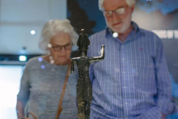 Two visitors look at a metal figurine that's inside a glass museum case