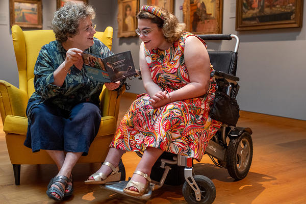 Visitors sitting together in gallery, one woman is smiling and chatting with her friend in a wheelchair 