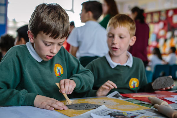 Two young school boys, in green jumpers, sit at a table and take part in a craft activity