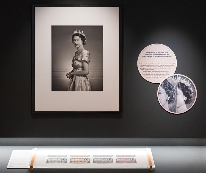 Money Talks exhibition gallery display of Queen Elizabeth II's portrait next to the a photo showing the devil in the hair pointed out and a display of the Canadian banknotes below