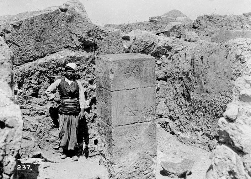 Black and white photo of Cretan worker next to pillar in Knossos Palace (West Pillar Crypt), 1900