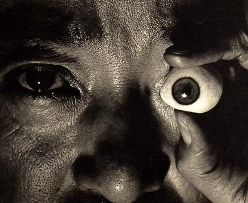 A man's face, he is holding a fake eyeball over his eye. Anxious Corridor,1940, by Surrealist artist Kansuke Yamamoto