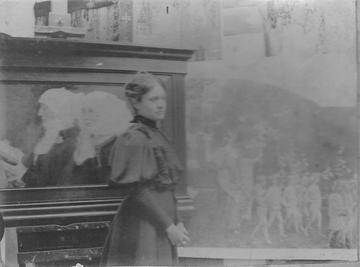 Blacka and white photograph of Elizabeth Sonrel standing by her painting