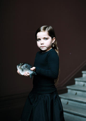 Tallulah and Jasmine, a photograph of a girl holding a fish against a black background with staircase on the right by artists Bettina von Zwehl, 2015