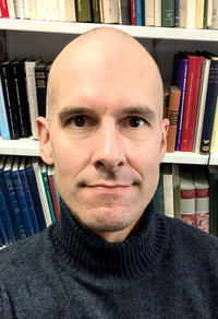 Profile photo of Ashmolean Research Fellow Joe Sheppard in front of a bookshelf